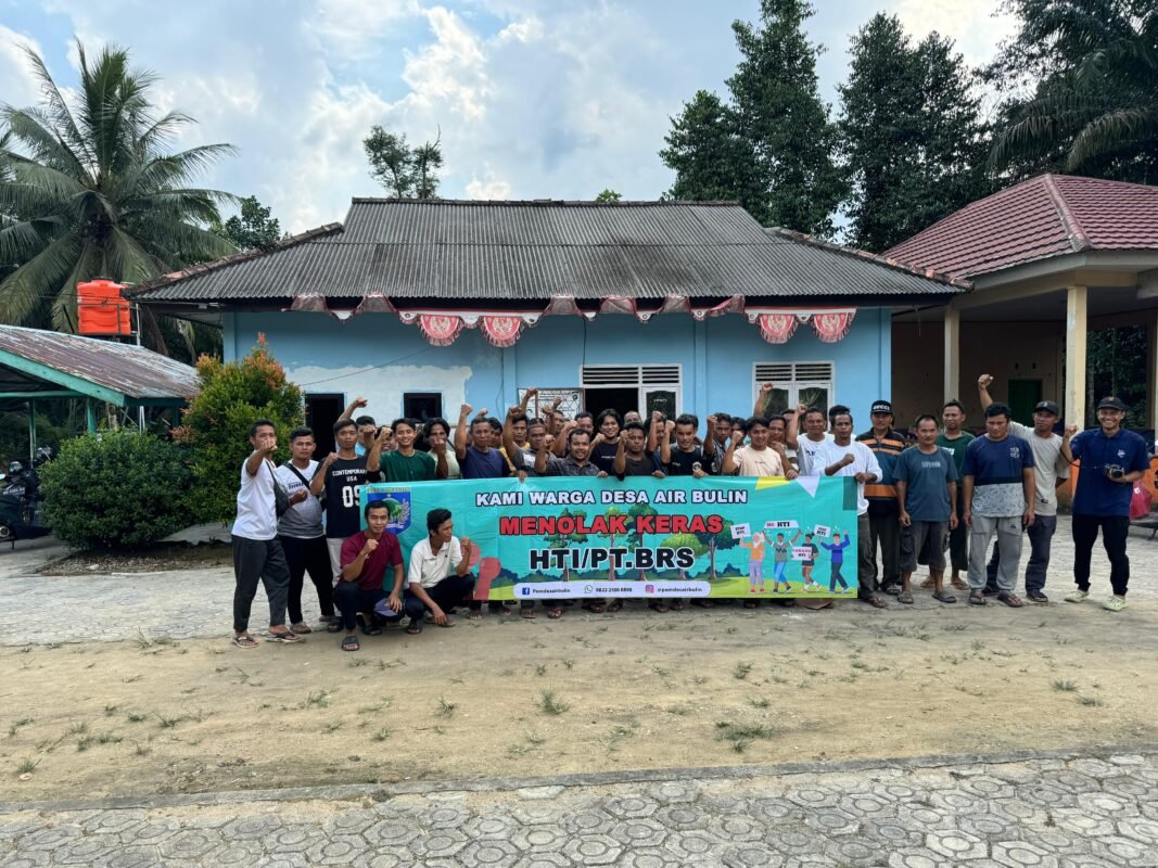 Sekelompok warga Desa Air Bulin berdiri bersama sambil mengangkat tangan dan memegang spanduk penolakan terhadap HTI/PT. BRS di depan bangunan desa.