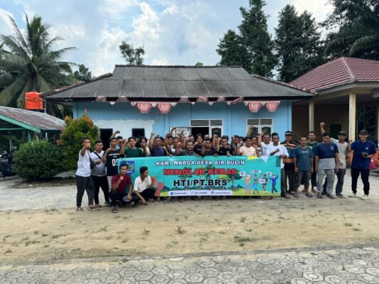 Sekelompok warga Desa Air Bulin berdiri bersama sambil mengangkat tangan dan memegang spanduk penolakan terhadap HTI/PT. BRS di depan bangunan desa.